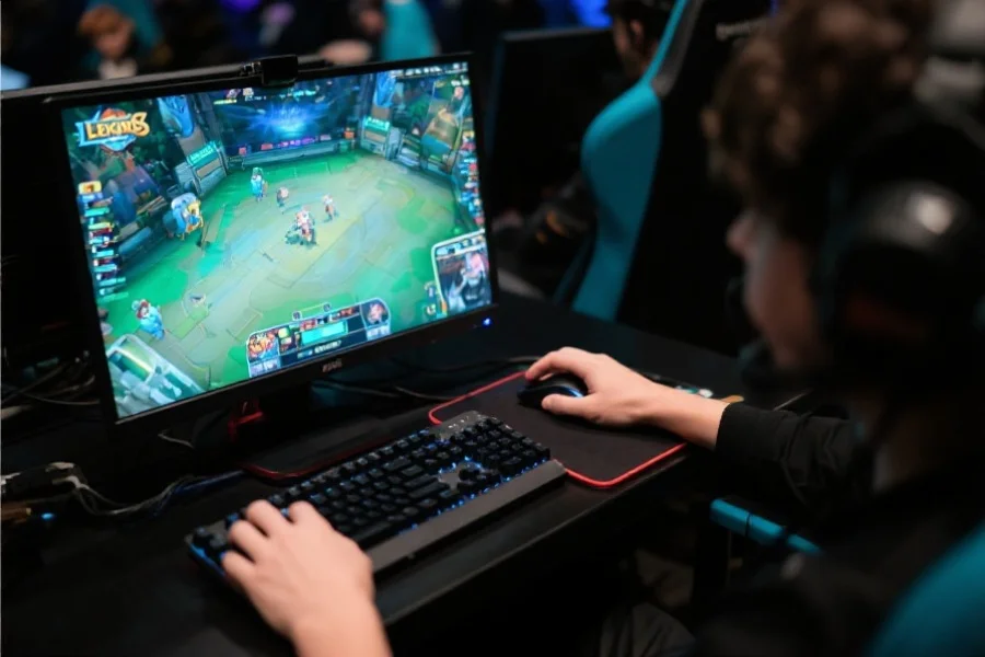 职业电竞选手专注操作电脑，手指灵活点击键盘鼠标，屏幕上显示英雄联盟比赛画面